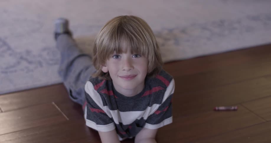 A young boy laying on the ground next to crayons