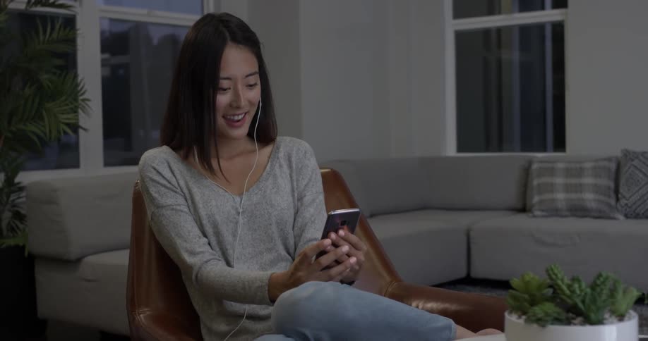 A woman puts headphones in as she sits in a living room at dusk