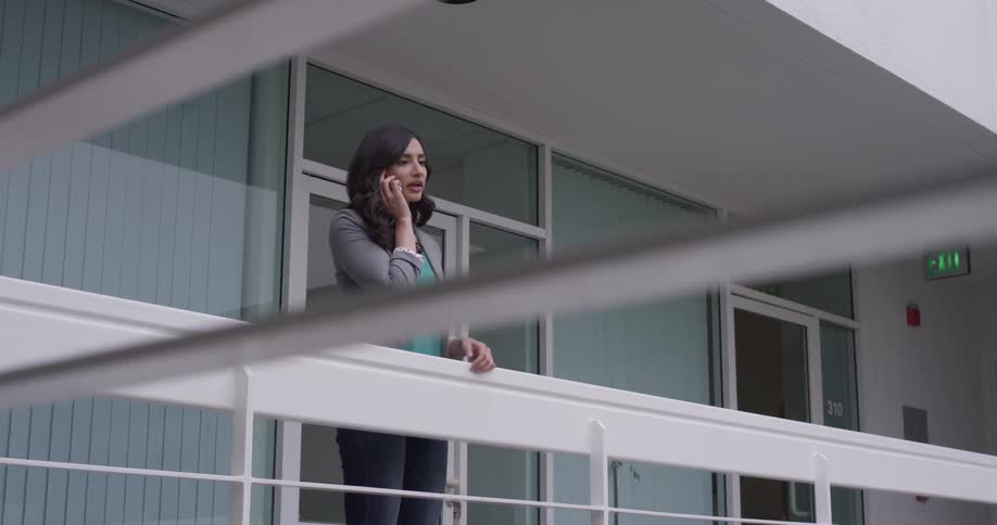 A woman stands on a balcony and talks on the phone
