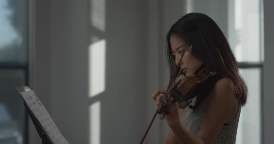 Woman is setting up some sheet music on the holder and staring reading the music while playing the violin and gets upset and throws the papers around