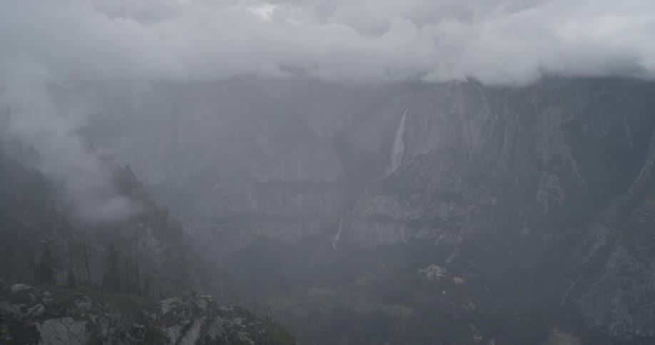 Clouds cover a mountain as a waterfall rushes from the middle of it