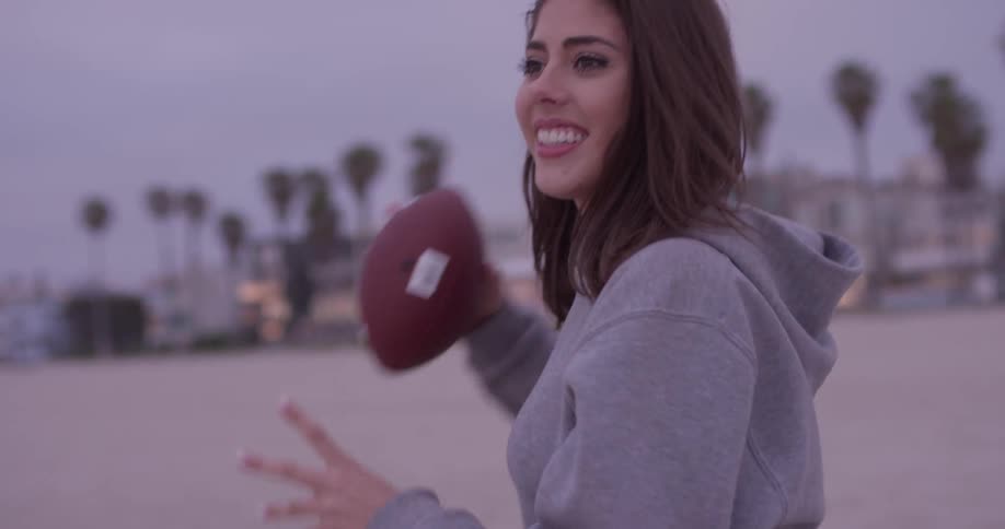 Smiling woman catches and throws the football on the beach