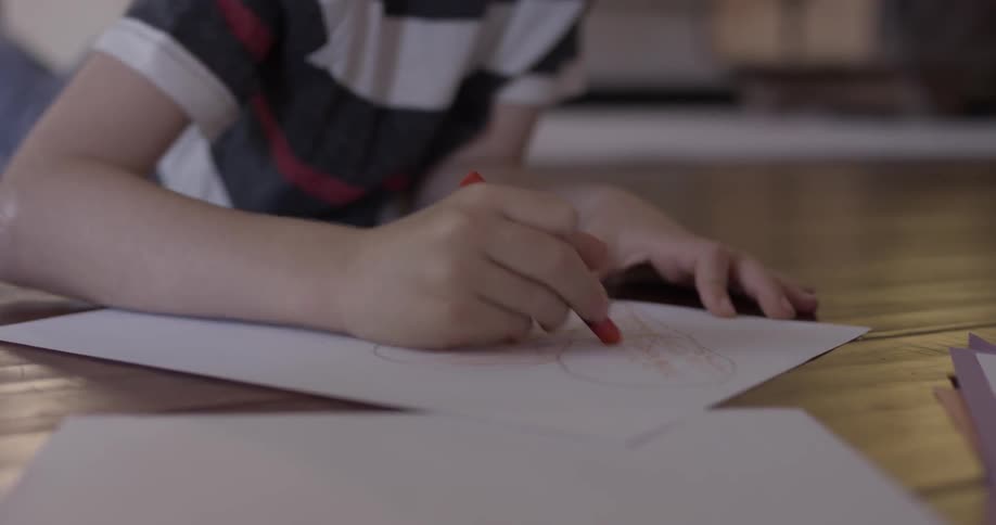 A child lays on the living room floor drawing on a sheet of paper with his crayons
