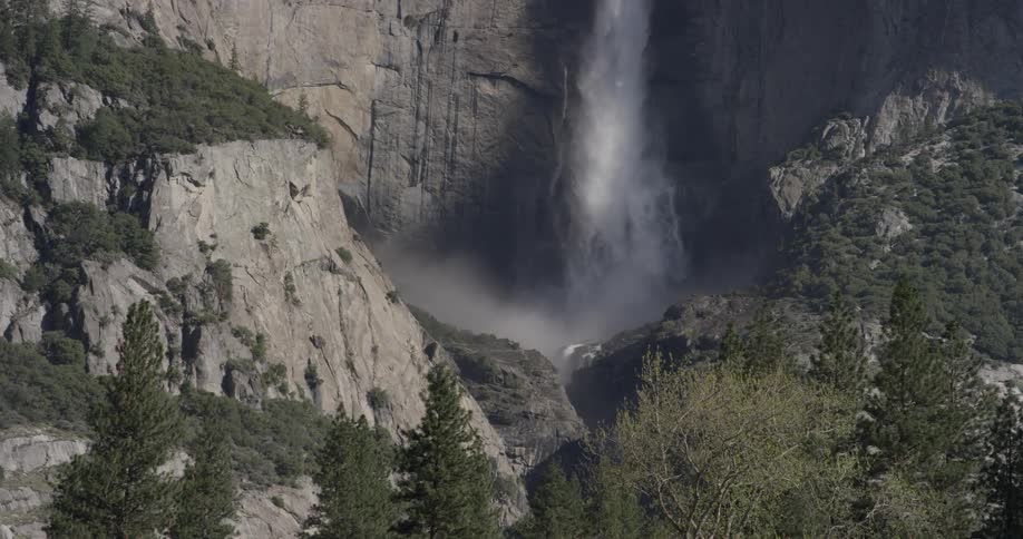 A waterfall coming off a cliff surrounded by trees and smaller cliffs on a sunny day