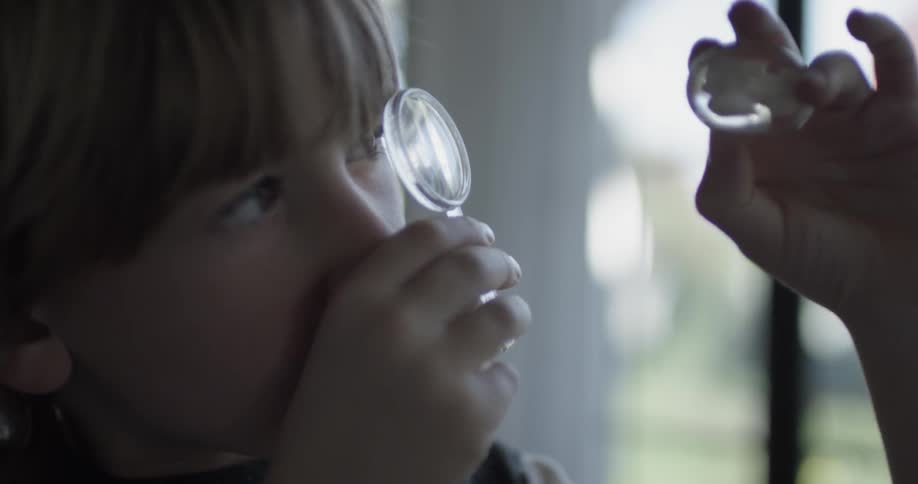 A child inspects a oval shaped glass object through a plastic magnifying glass in his home