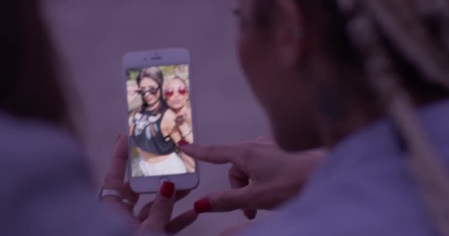 A woman showing pictures of herself and another woman on her phone to someone else