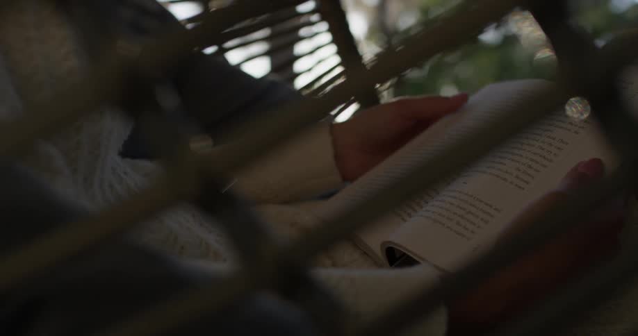 A woman reads a book as she sits in a wicker chair under the sun