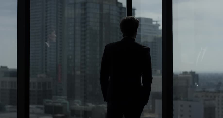 A man walking in a high rise building looking out the window at the view of downtown