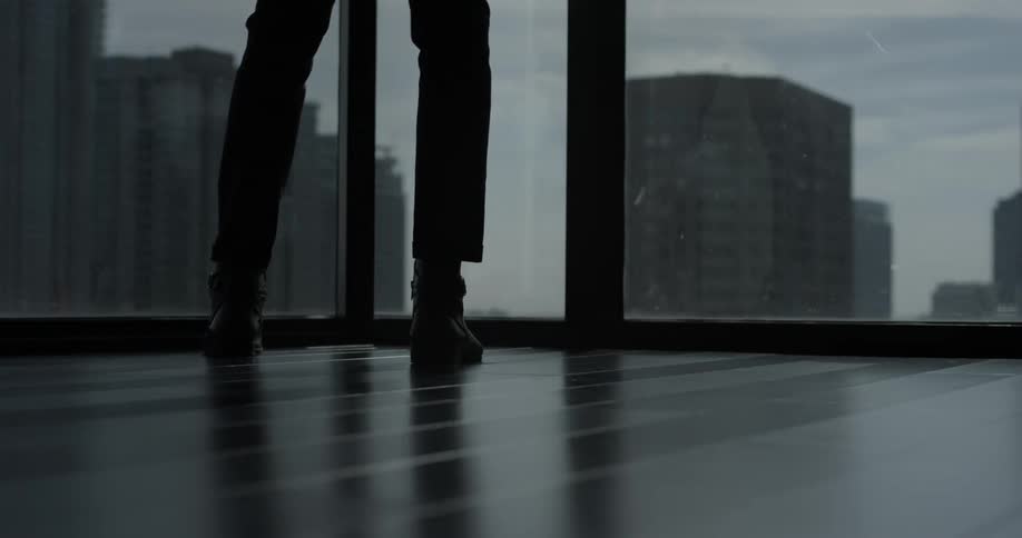 A person in a high rise walks towards windows that open the view to other tall buildings