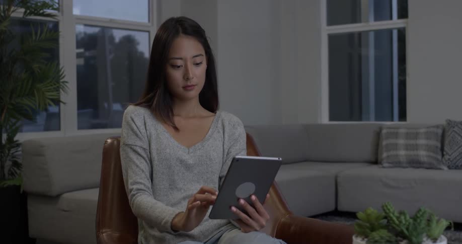A woman is swiping through her tablet while sitting on a chair