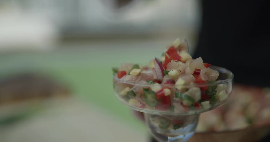 A chef wearing black gloves piles ingredients into a clear glass cup