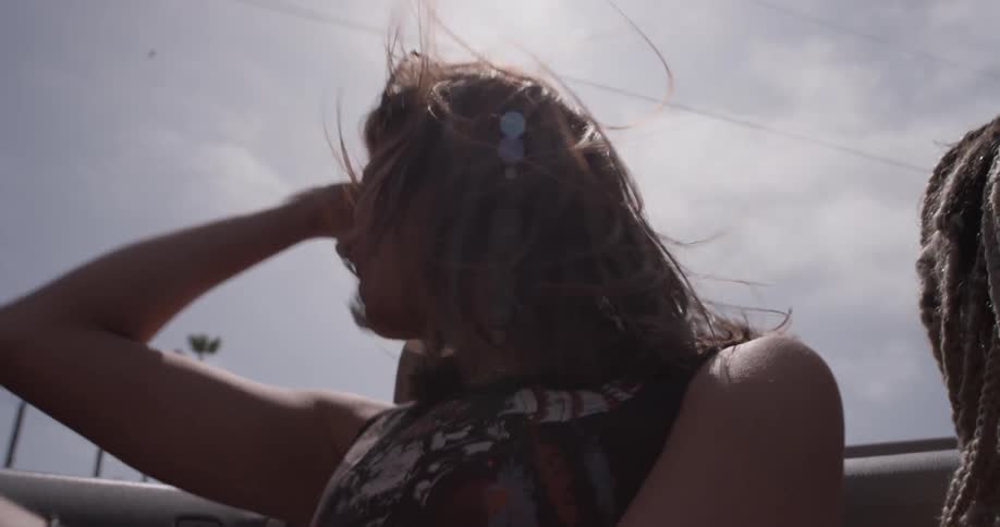 Woman smiles and dances in a convertible on a sunny day