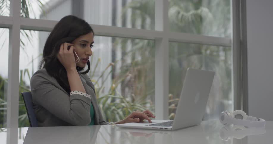 A woman talking on a phone using a laptop