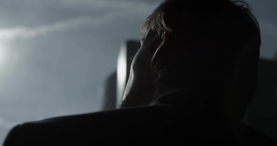 A man stares out a window at the sun and some contrails that have formed in the sky