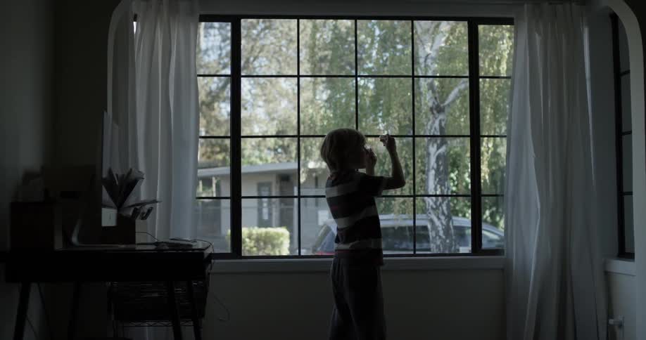 Child excitedly rushes to the window to see an object through a magnifying glass in the living room