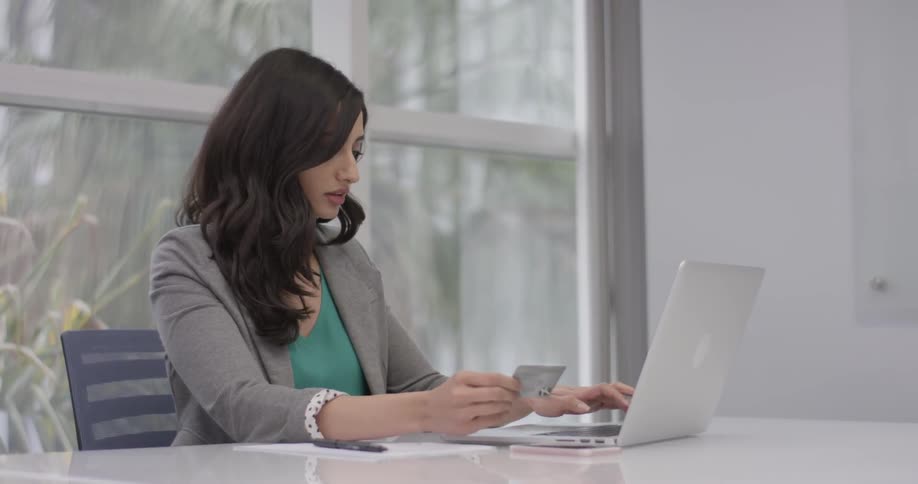 A woman picks up a card, and starts typing on a laptop