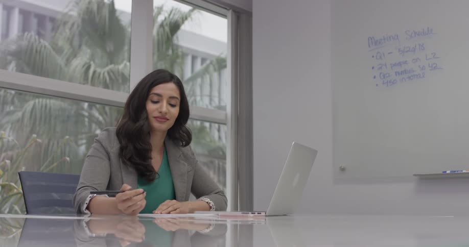 Woman dressed in business clothing works at a laptop and writes on a paper at a desk