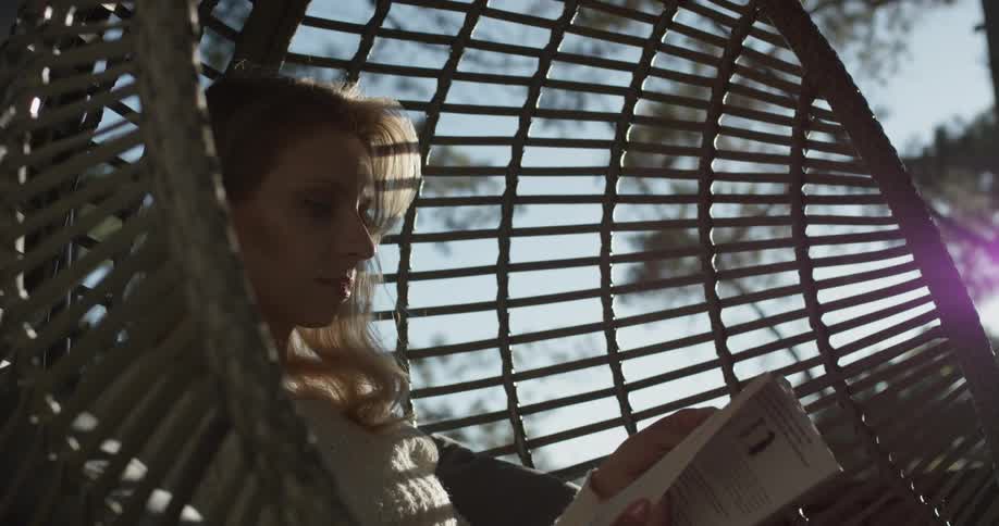 Woman reads a book while sitting in a small cylindrical swing