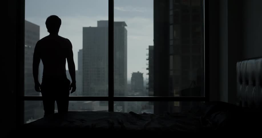A man gets out of bed and looks out over the city skyline