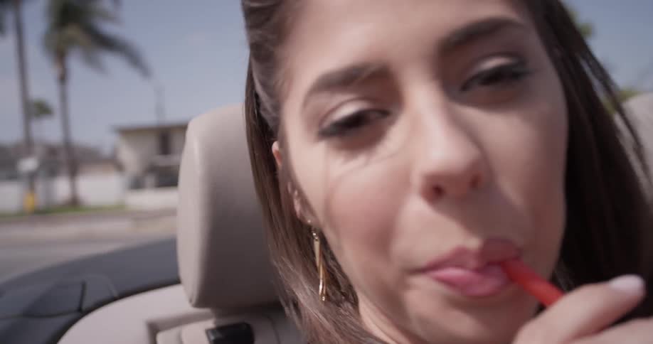 A woman dances in the back seat of a convertible as she takes a drink