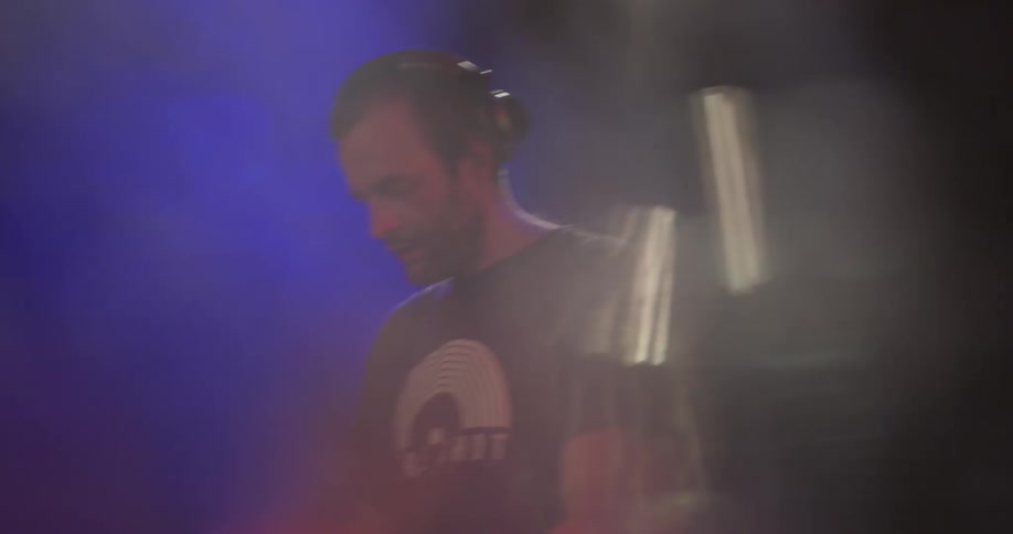 A man wearing headphones does a dj performance in a club lit with red and blue lights