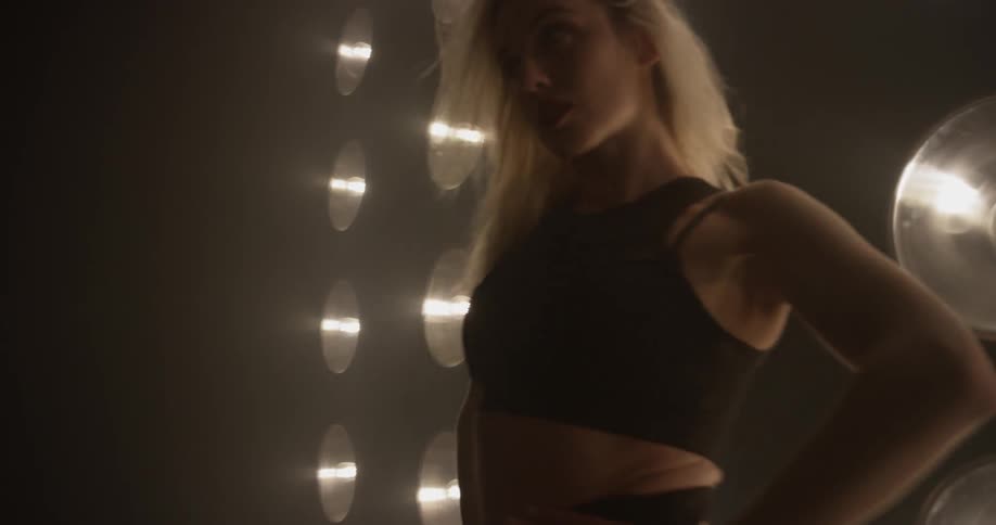 A woman stands in front of many lights while dancing