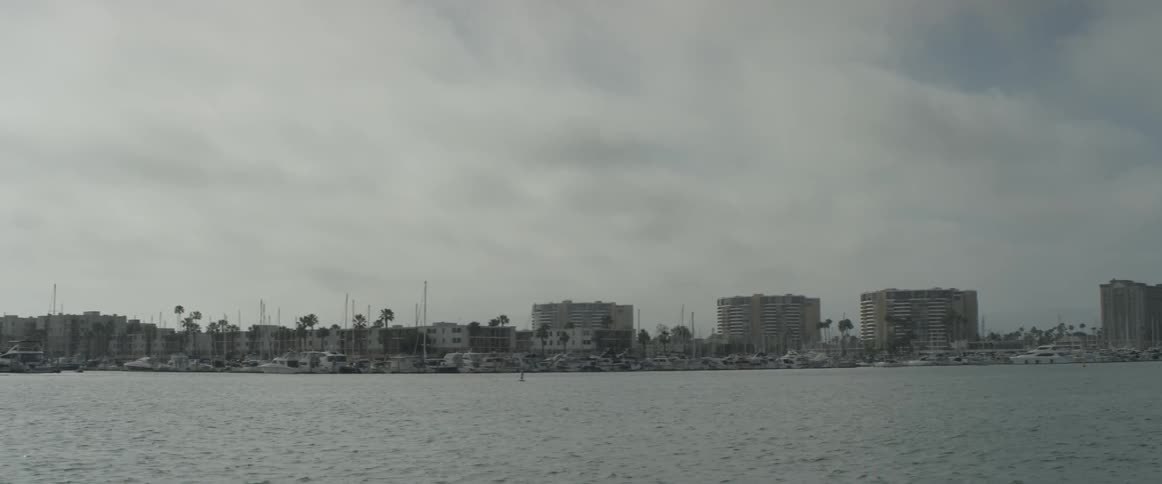 A cloudy not very sunny day out on the water of a city with plenty of boats lining the shore