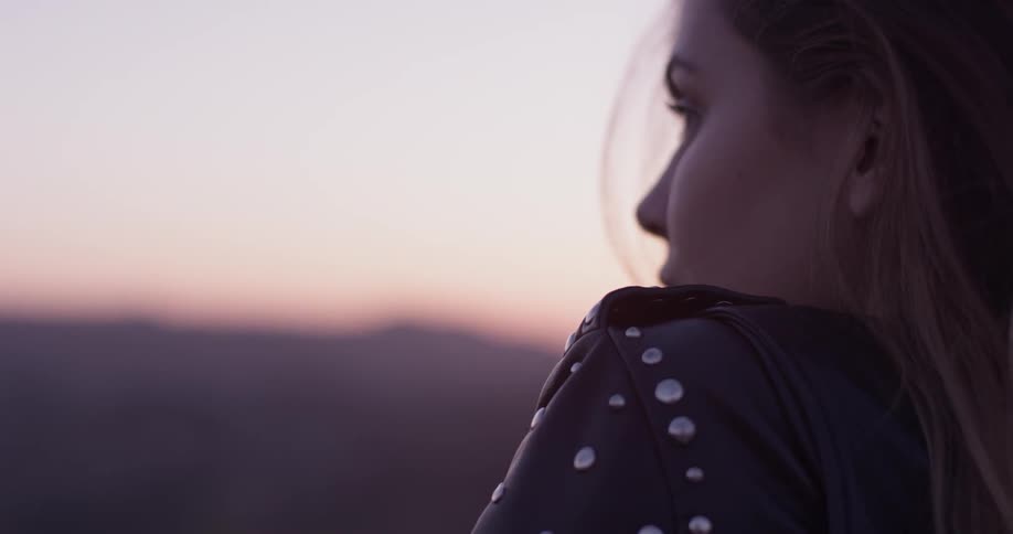 A woman standing at the top of a mountain at sunset