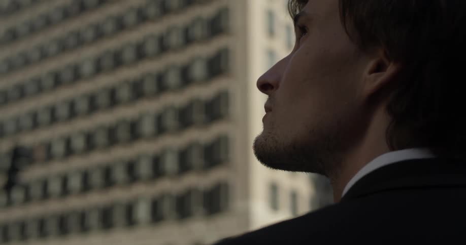 A man stands before tall building on a sidewalk in the middle of downtown of a large city