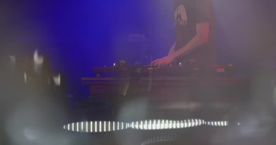 A man at a club does a dj performance live with red and blue shining lights