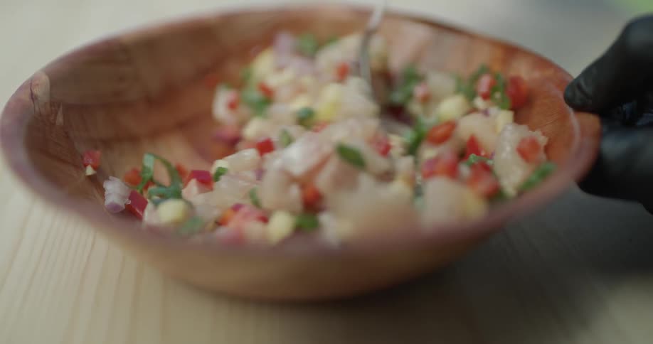 A blend of different vegetables and spices is stirred in a wooden bowl on the table