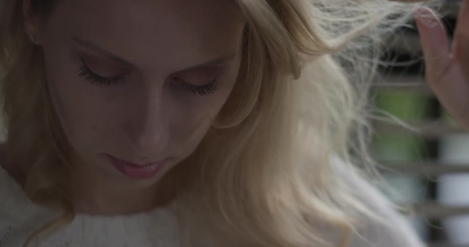 A blonde haired woman looks down and plays with her hair
