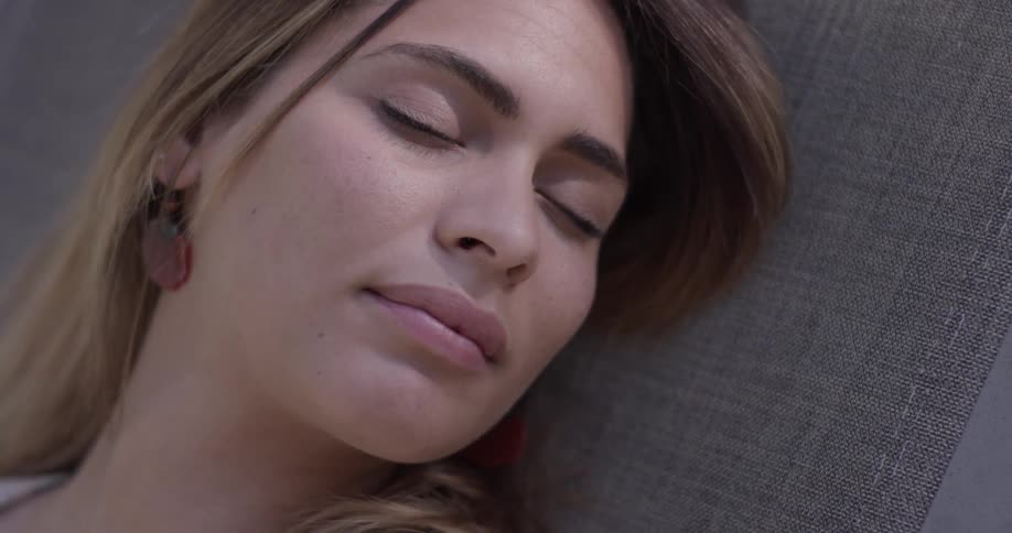 A woman lays on a cloth wearing earrings laying down in the sun closing her eyes