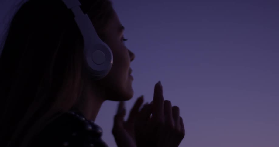 Woman putting on headphones at dusk