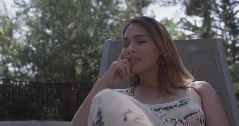 Woman sits in a lounge chair on a tree lined patio