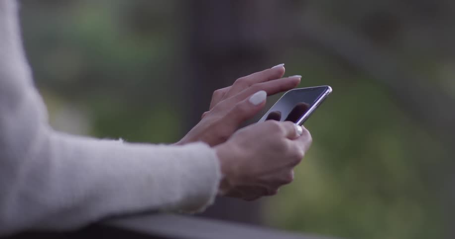 A woman swipes on a smartphone as she leans on a railing
