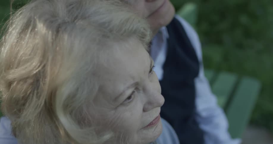 An elderly man and women sit on a bench at the park and enjoy their time together