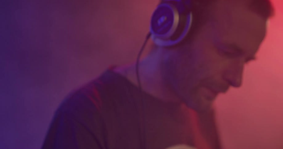 A man wears headphones and bobs his head doing a dj performance in a red and blue lit room