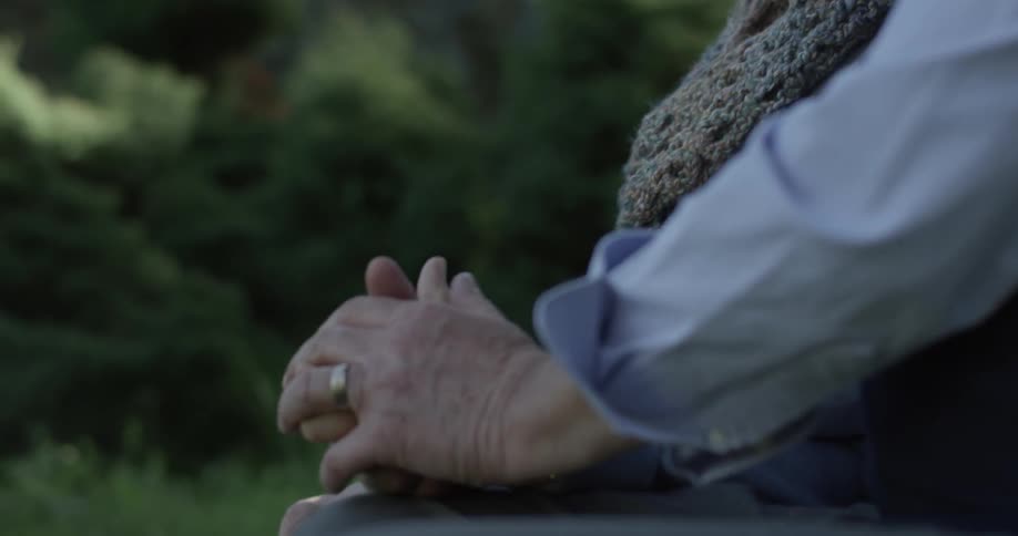A man and a woman who are likely a couple sit at a park bench and hold each others hand while looking at each other
