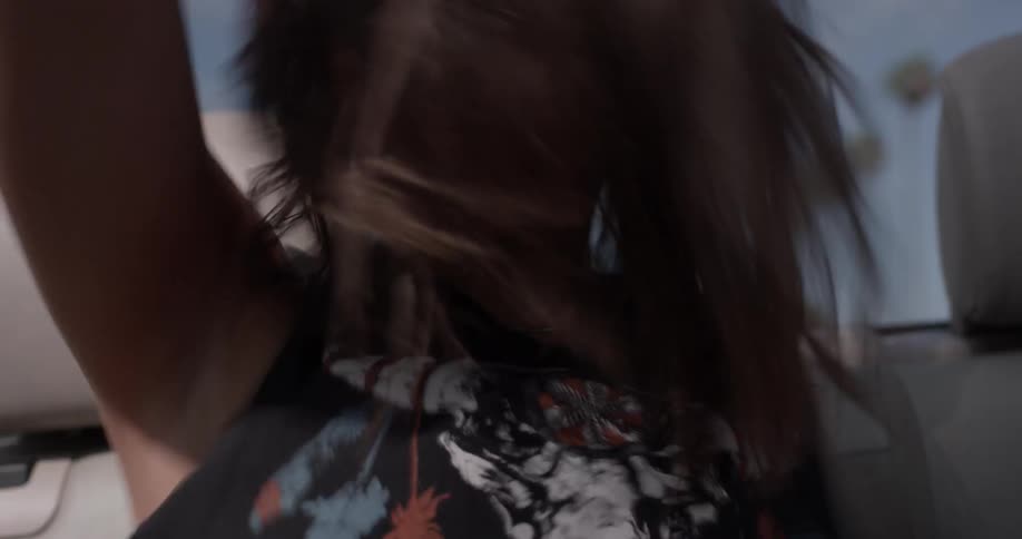 Two women dance in the back seat of a convertible