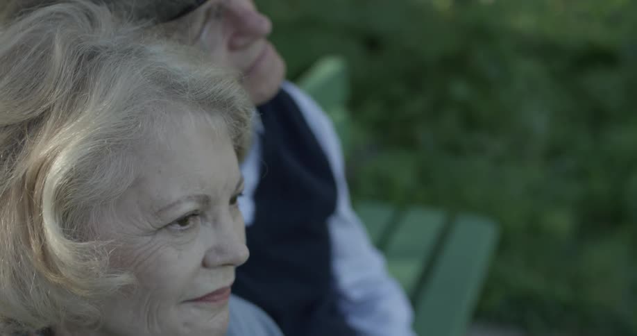 Elderly man and woman sit on park bench in the daylight