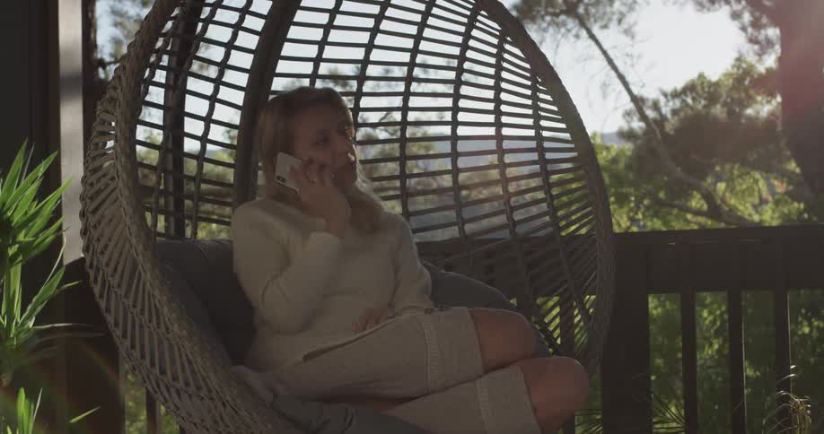 Women answers the phone in a patio furniture chair she is sitting on on a bright sunny day with the shining sun