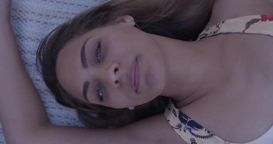 A woman lays on her back looking up with a sultry smile