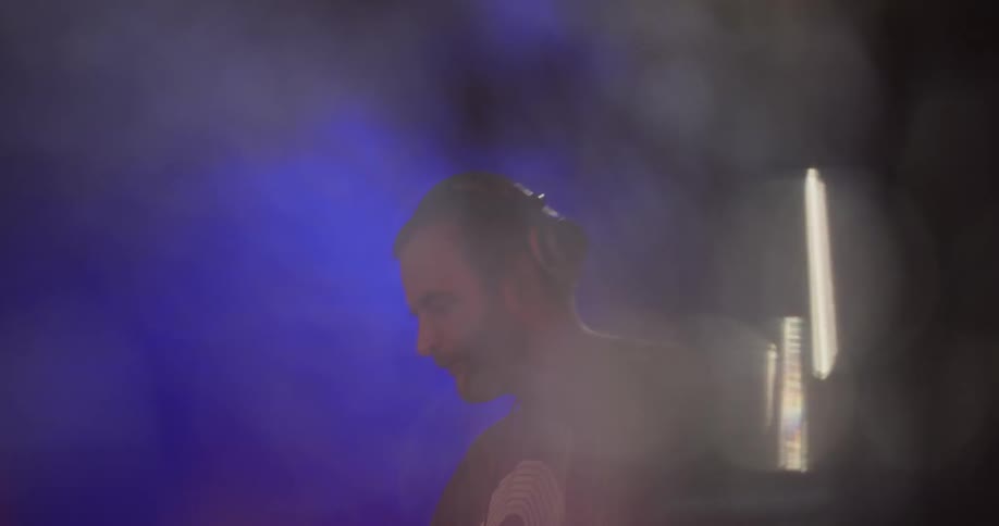 A man performs a dj session at a club with red and blue lights shining above him