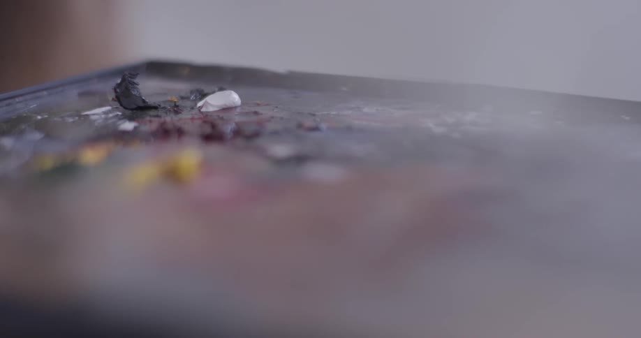 An artist is squeezing a dab of oil paint onto a palette and mixing it with a knife