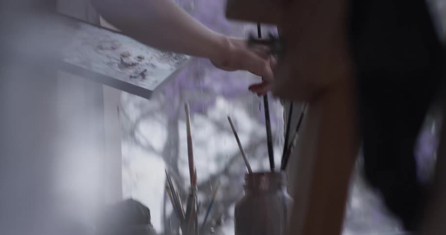Woman picks up paints and a brush and gets ready to paint a picture