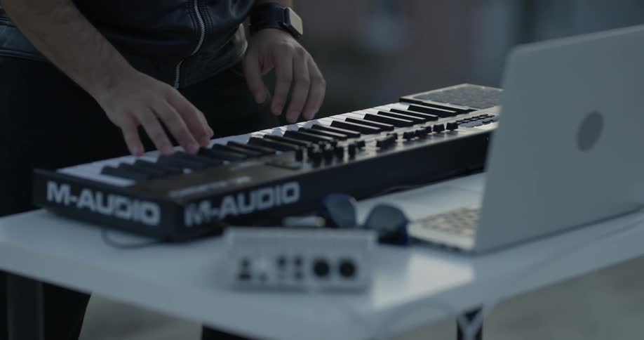 A man plays a keyboard that's sitting on a table in front of a laptop