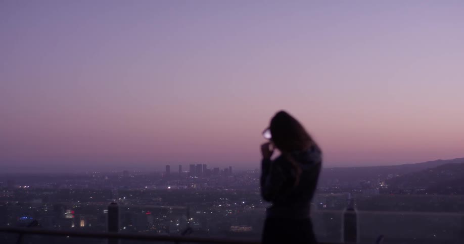 A woman takes a picture of a city that's illuminated by a striking purple sunset
