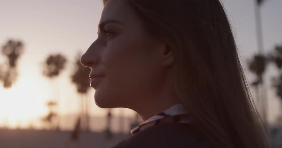 A closeup of a woman staring out into an an unknown area at the beach with her hair blowing in the breeze