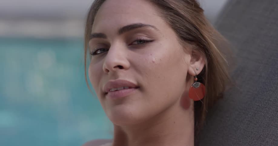 A woman sits by a pool smiling over brightly
